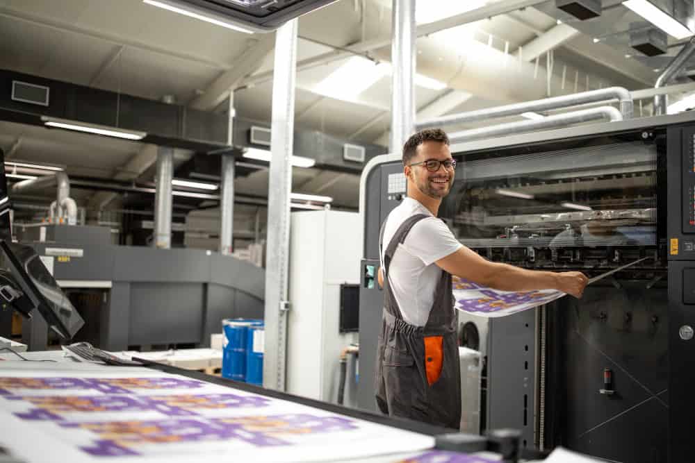 Métiers de l'emballage : un membre souriant de notre équipe chez Leca Graphics, expert en packaging de luxe, opérant une presse d'impression offset.