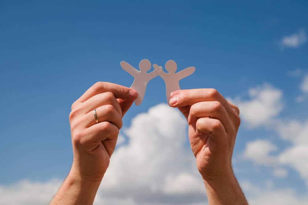 Hands holding two white paper figures against the sky, symbolizing collaboration and teamwork, key values for packaging printers.