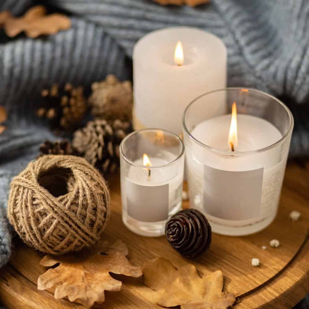 Luces de velas decorativas para ambientes cálidos y acogedores, ideales para centros de mesa y decoración autumnal en pack de packaging de lujo. Elegant scented candles in glass jars surrounded by rustic decor, demonstrating the versatile structural design capabilities of our Custom Luxury Packaging.