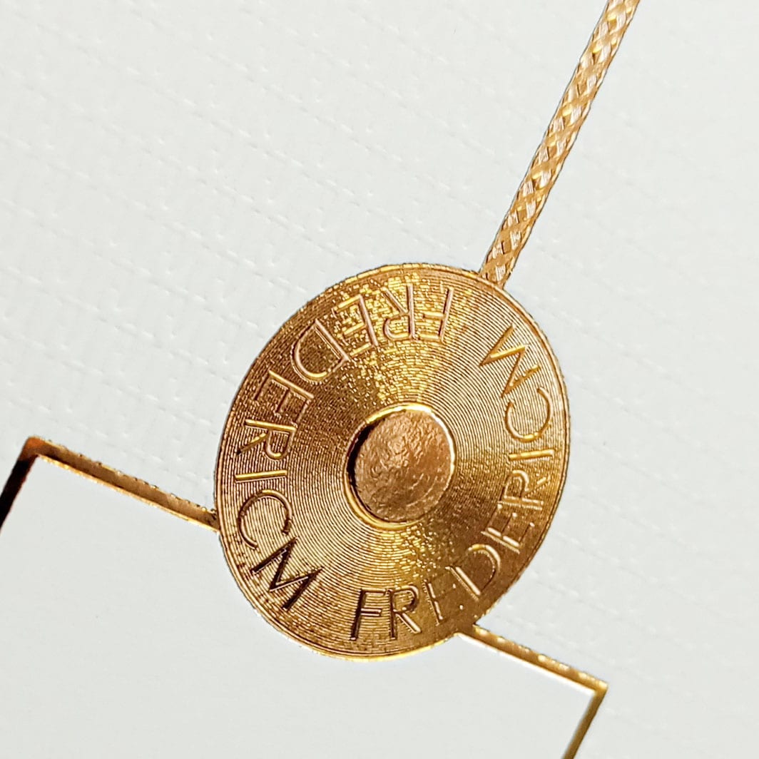 Sello circular con micro estampados dorados que muestran tipografía minúscula de alta definición.