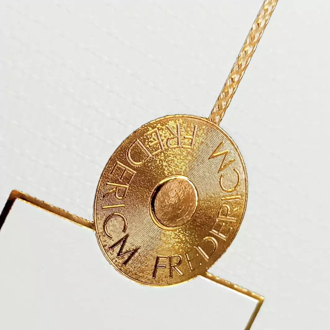 Placa de metal dorada con grabados y cordón decorativo, microstamping.